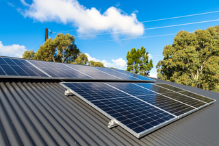 Solar panels on a gray metal roof under a blue sky with trees in the background