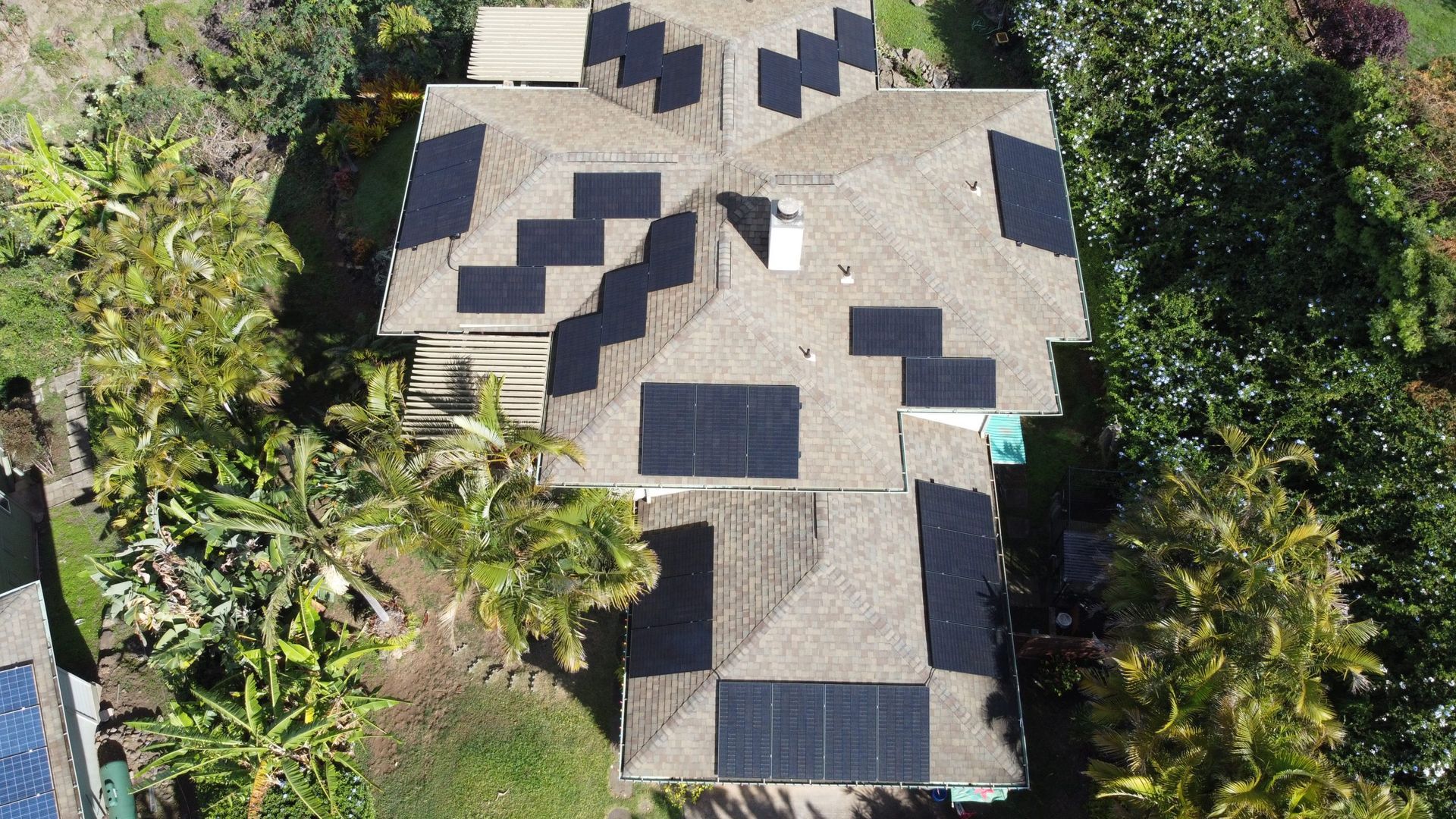 Aerial view of a house roof with multiple solar panels surrounded by trees.