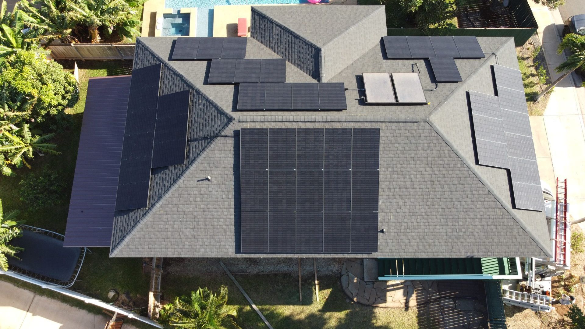 Aerial view of a house roof with multiple solar panels and dark gray shingles.