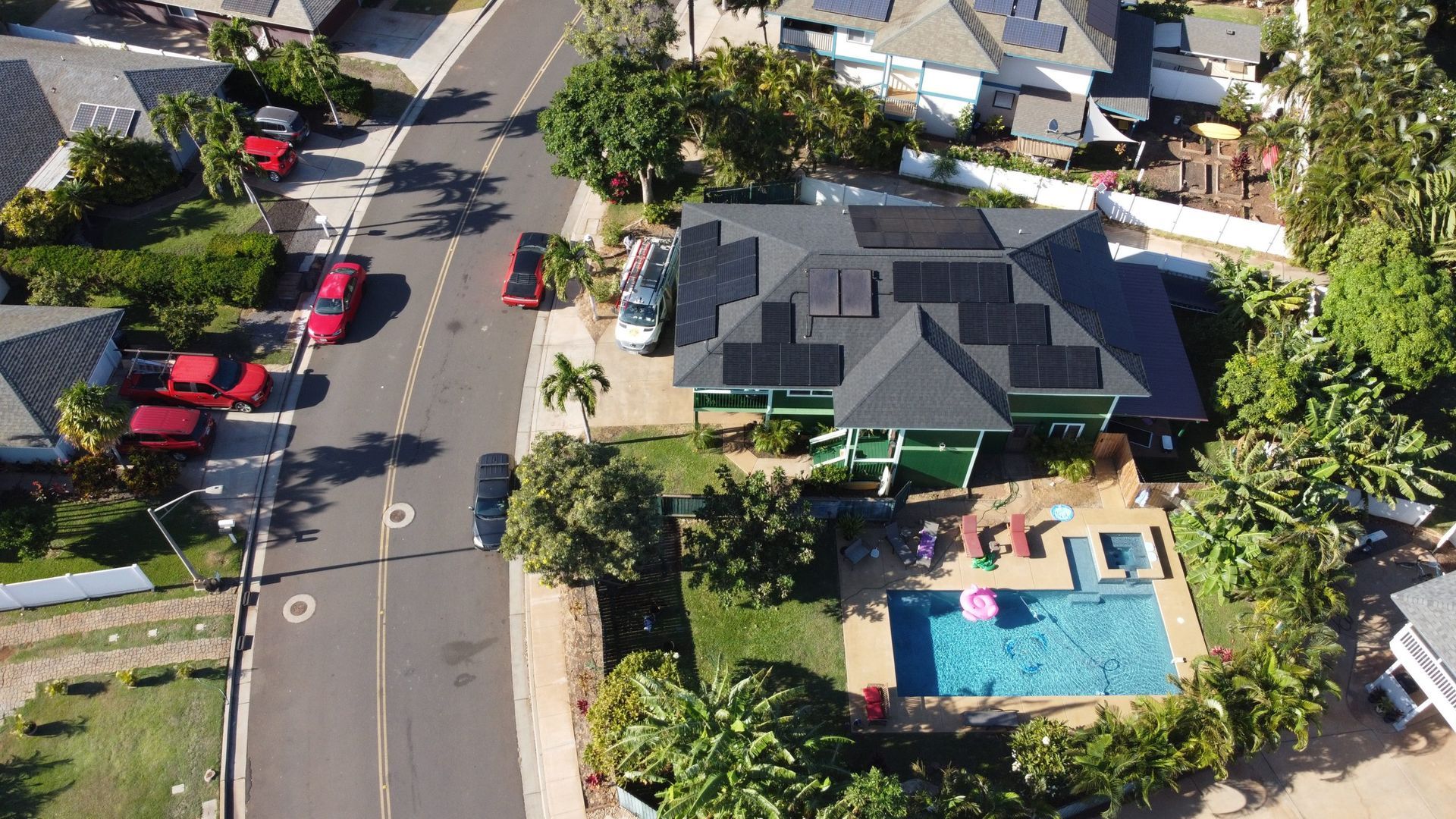 Aerial view of a suburban street with houses, parked cars, and a home with a backyard pool.