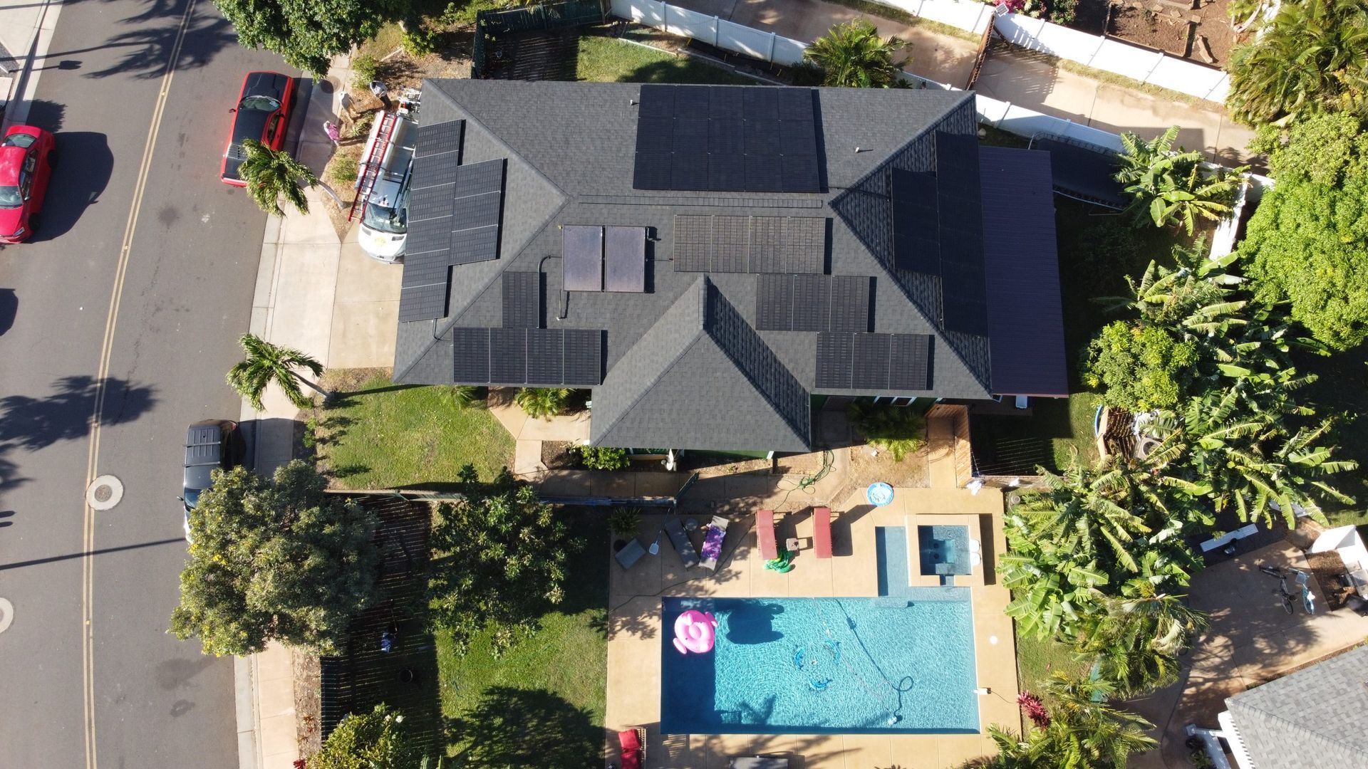 Aerial view of a house with a dark roof, backyard pool, patio, and surrounding trees.