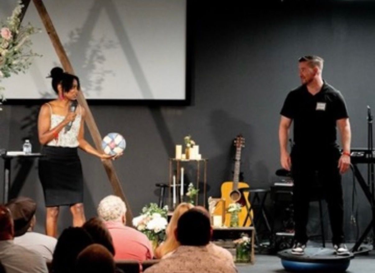 Chad and Sarah-Gayle Galbreath on stage in front of a floral arch with an audience in the foreground