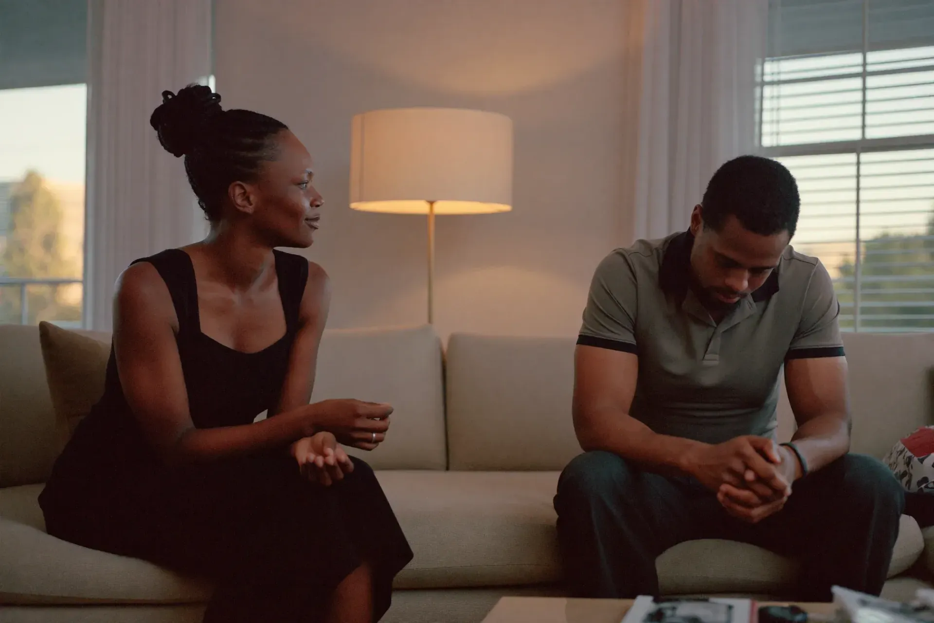 Married couple sitting apart on a sofa in the evening, one talking and the other looking down, a common sign a Gilbert couple needs counseling