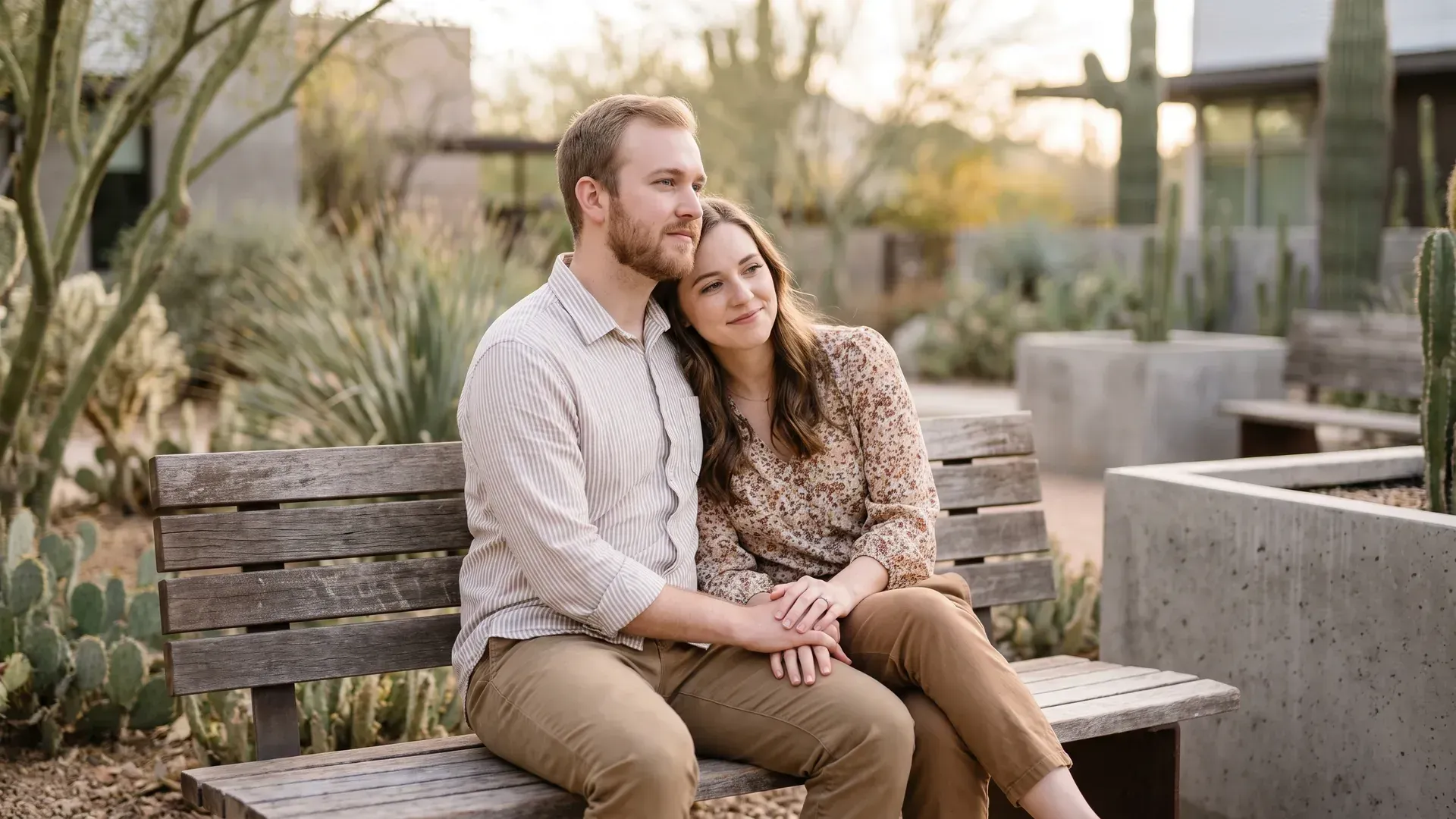 Young married couple sitting close together on a bench in a quiet desert garden courtyard, holding hands, calm and hopeful