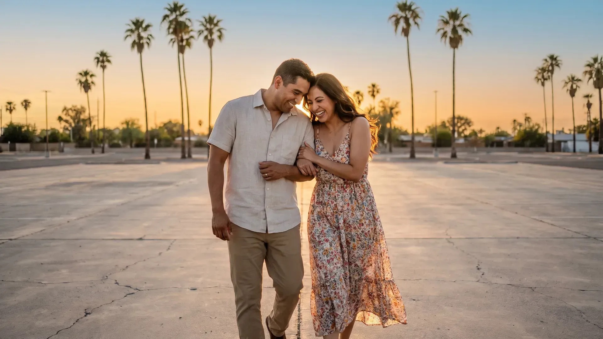 Latino married couple in their mid thirties walking together on a wide empty plaza at golden hour, laughing and leaning into each other, palm trees behind them