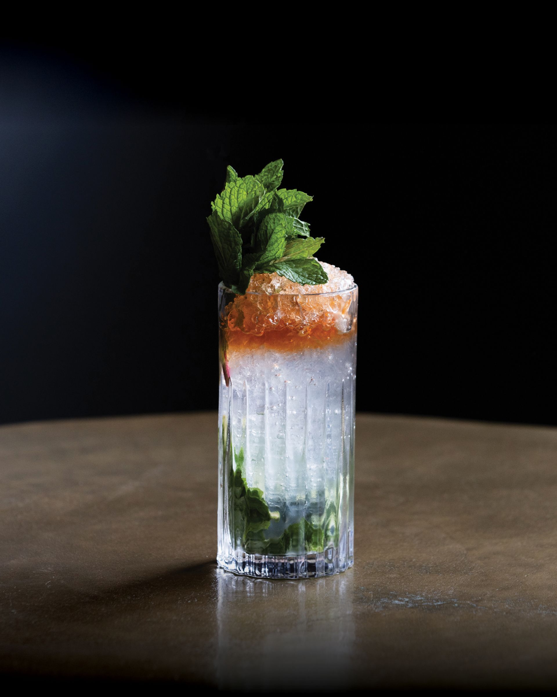 A tall glass filled with a drink and mint leaves on a table.