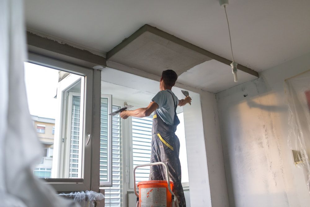 A Man Is Standing on A Ladder Plastering the Ceiling — MJ Watson Construction and Maintenance in Wagga Wagga, NSW