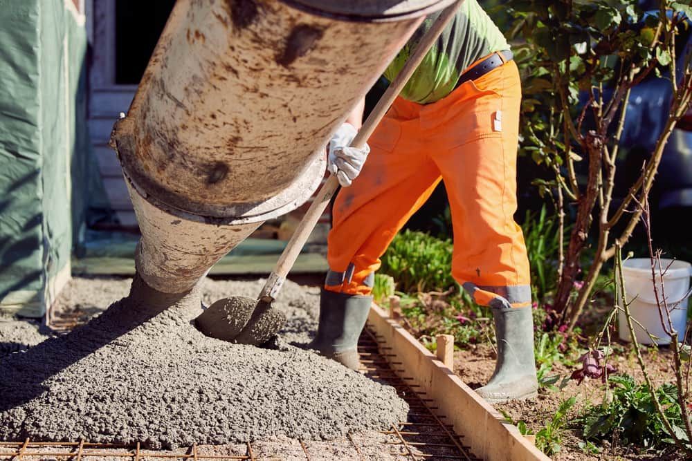 A Man Is Pouring Concrete Into a Hole with A Shovel — MJ Watson Construction and Maintenance in Wagga Wagga, NSW
