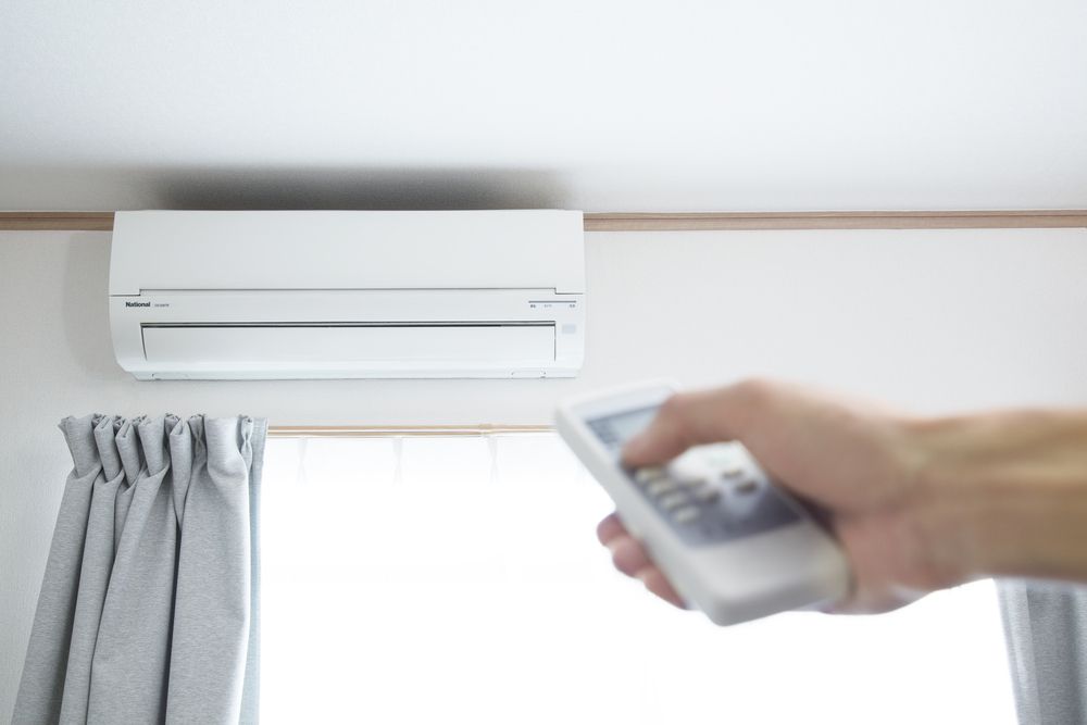 Hand Holding Remote, Adjusting Wall-mounted AC — Cumming Airconditioning & Sheetmetal in Ryan, QLD