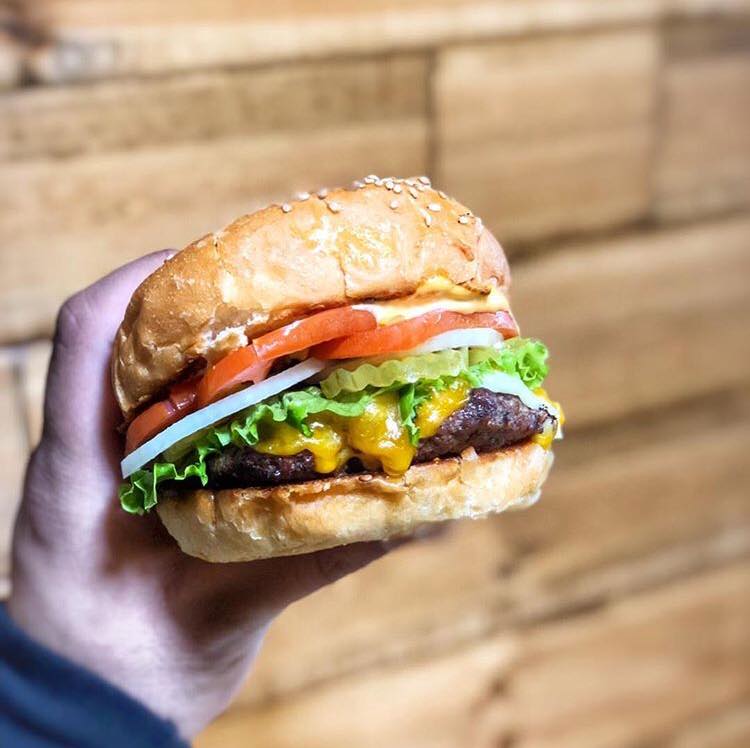 A person is holding a hamburger with lettuce tomato and cheese