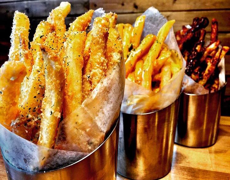 Three buckets of french fries are sitting on a wooden table.