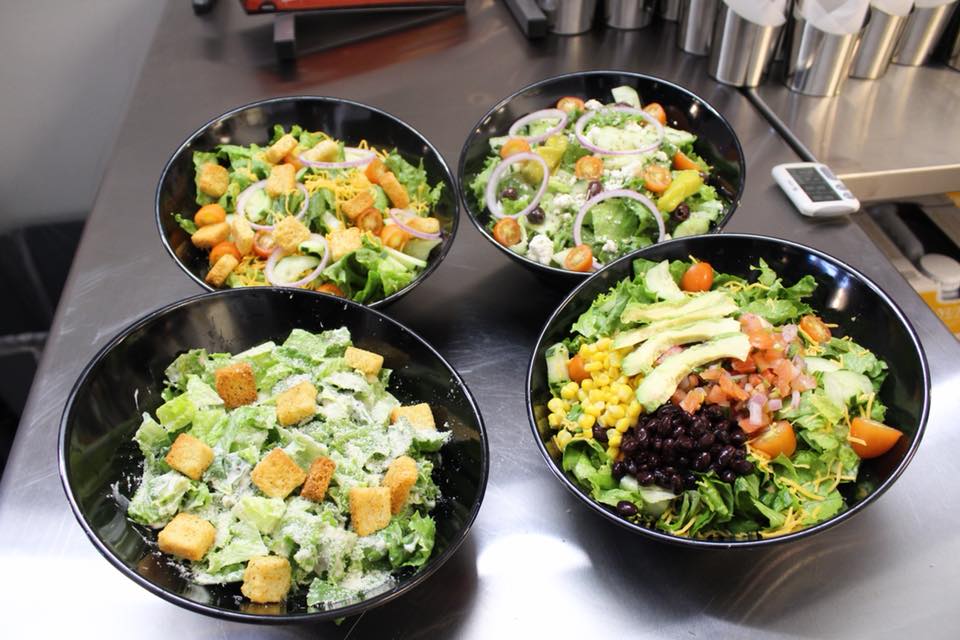 Four bowls of different salads are on a counter