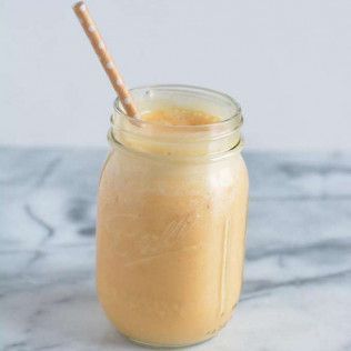 Orange smoothie in a mason jar with a straw.