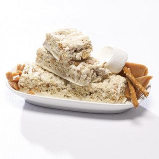 White-frosted dessert bars stacked on a white plate with marshmallows, pretzels, and caramel candies.
