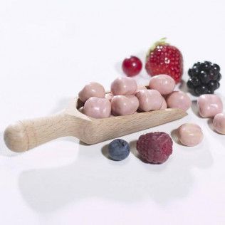 Pink candies spilling from a wooden scoop, with assorted berries scattered on white.