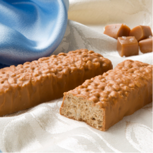 Two caramel-covered candy bars and caramel candies on a white cloth, blue satin in background.