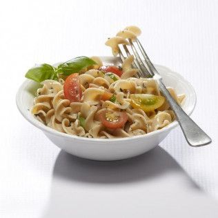 Pasta salad with tomatoes and basil in a white bowl, fork.