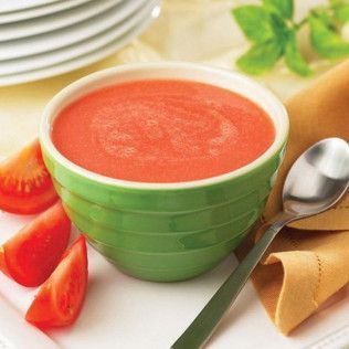 Bowl of smooth, pink tomato soup; a spoon rests beside it, with tomato slices and a folded napkin.