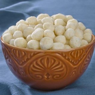 Bowl of white, puffy, round snacks in an embossed brown bowl on a blue surface.