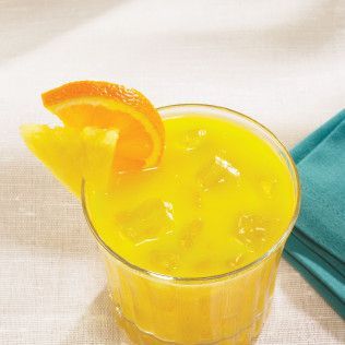 Glass of orange juice with ice cubes, garnished with an orange slice, on a white tablecloth.