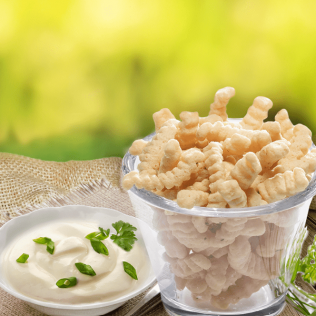 Bowl of wavy, light-colored snacks with a bowl of white dip, garnished with green herbs, outdoors.
