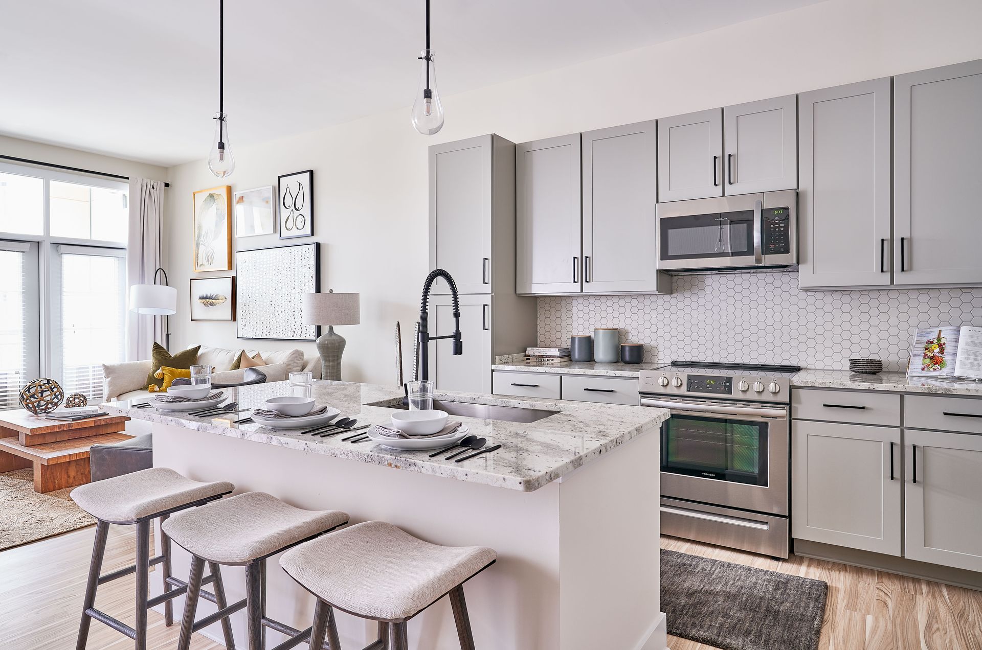 Modern kitchen with light gray cabinets, stainless steel appliances, and a granite countertop island with bar stools.