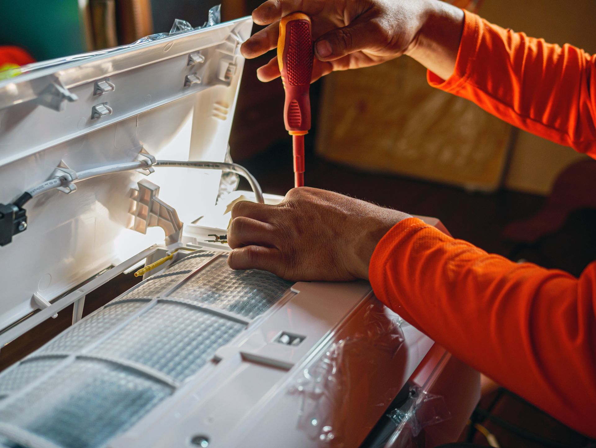 Technician using a screwdriver to repair a white appliance with orange interior parts