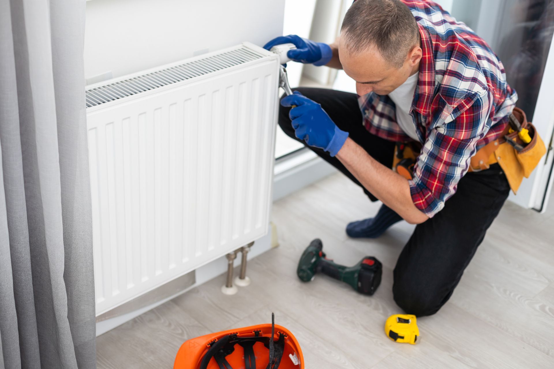 Technician installing a white radiator with tools in a room with light wood flooring
