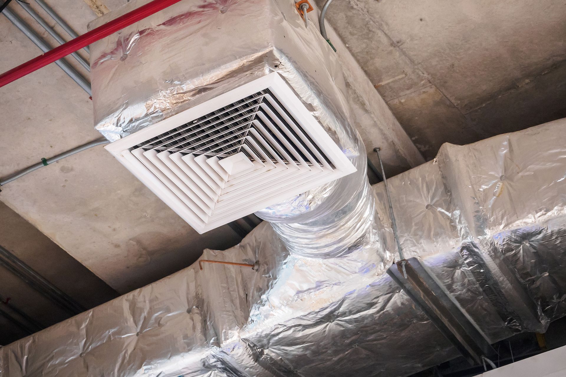 Ceiling HVAC vent with ducting and insulated metal pipes in an industrial building
