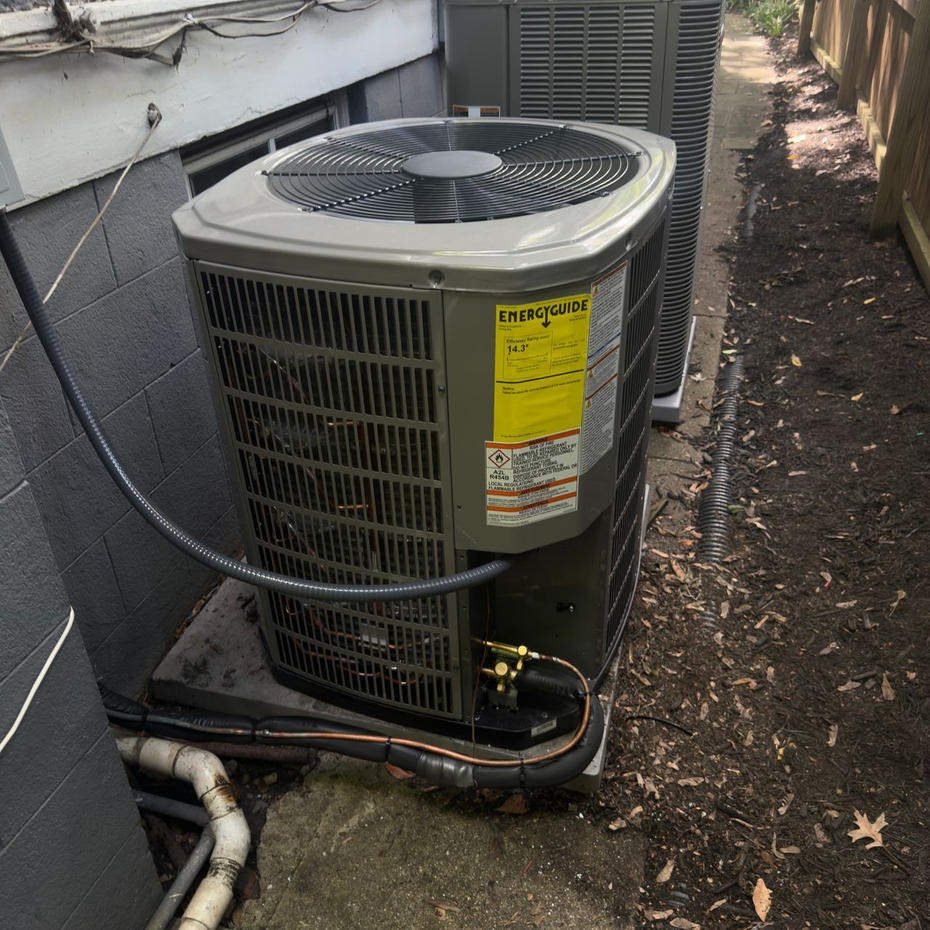 Outdoor air conditioner unit beside a house, with a yellow warning label and visible pipes.