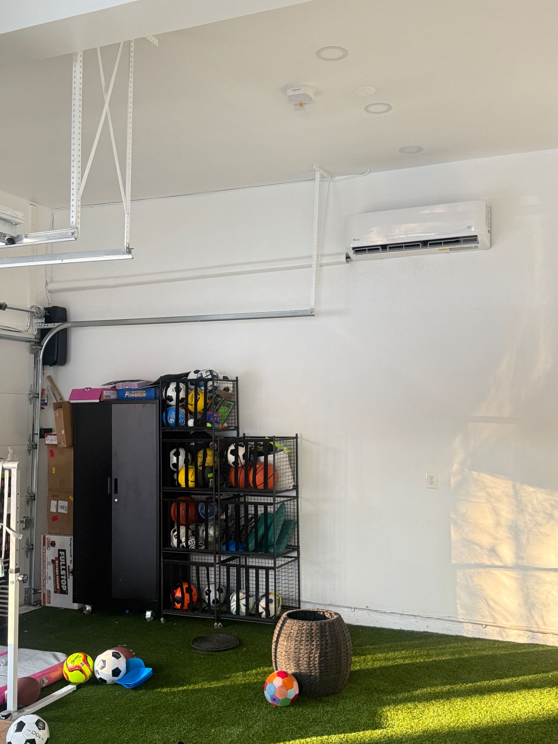 Indoor play area with artificial grass, toy balls, shelves, and a wall-mounted air conditioner