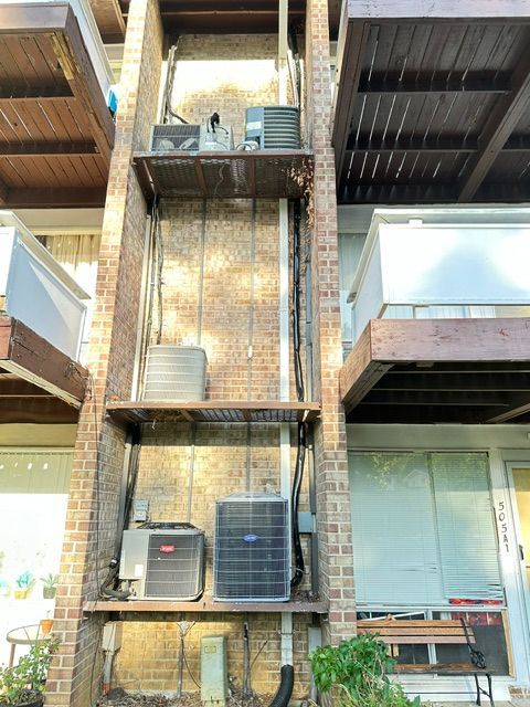 Brick building facade with stacked outdoor AC units and metal balconies above a glass storefront
