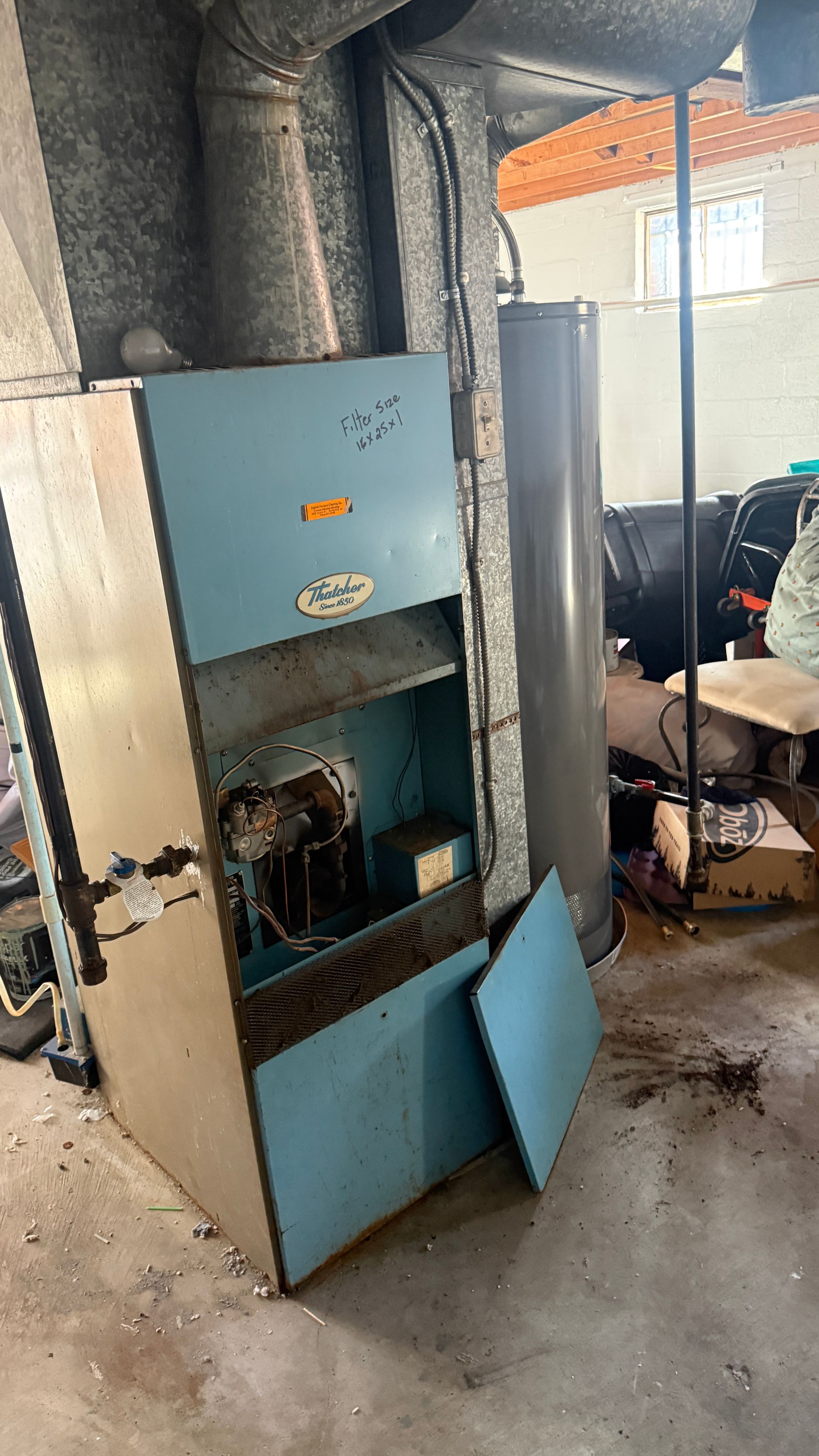 Blue industrial furnace with open door in a dusty workshop, surrounded by ducting and tools.