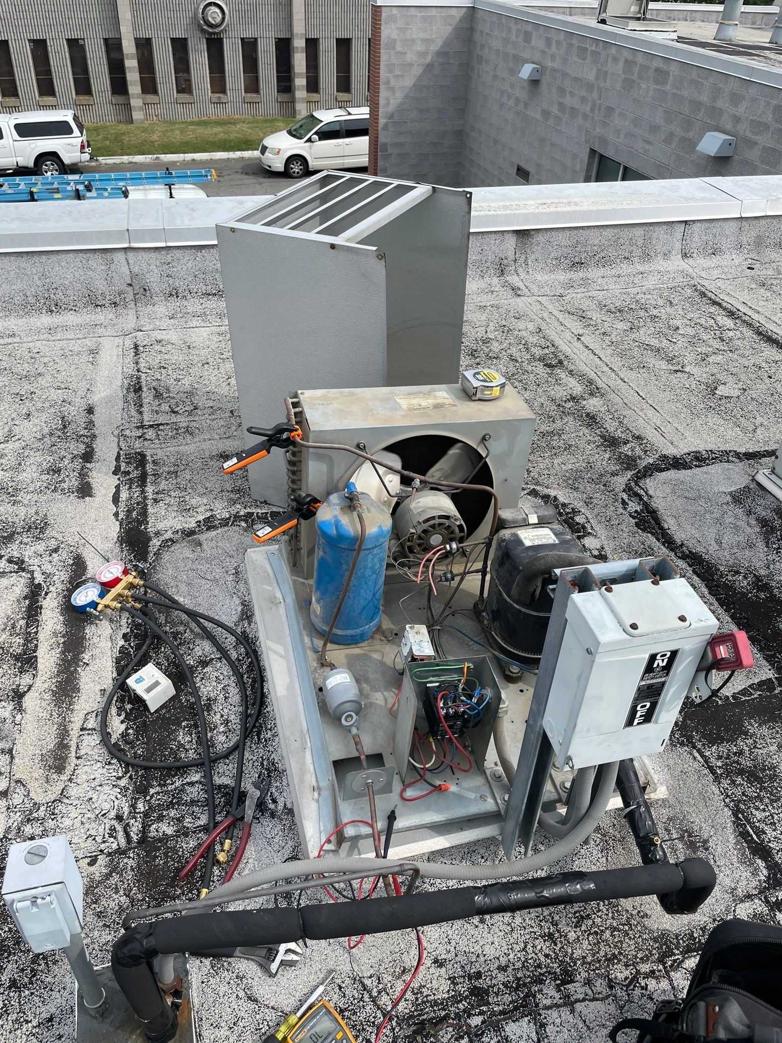 Rooftop HVAC machinery with ducts, pipes, and control boxes beside a gray wall