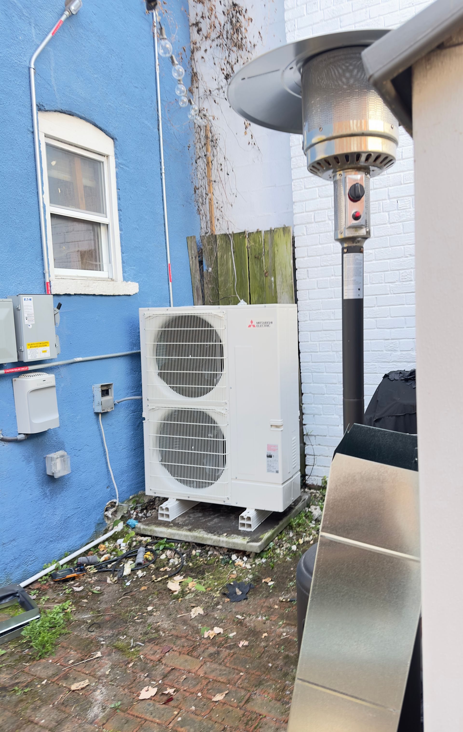 Technician cleaning a wall-mounted air conditioner with a brush in a bright room.