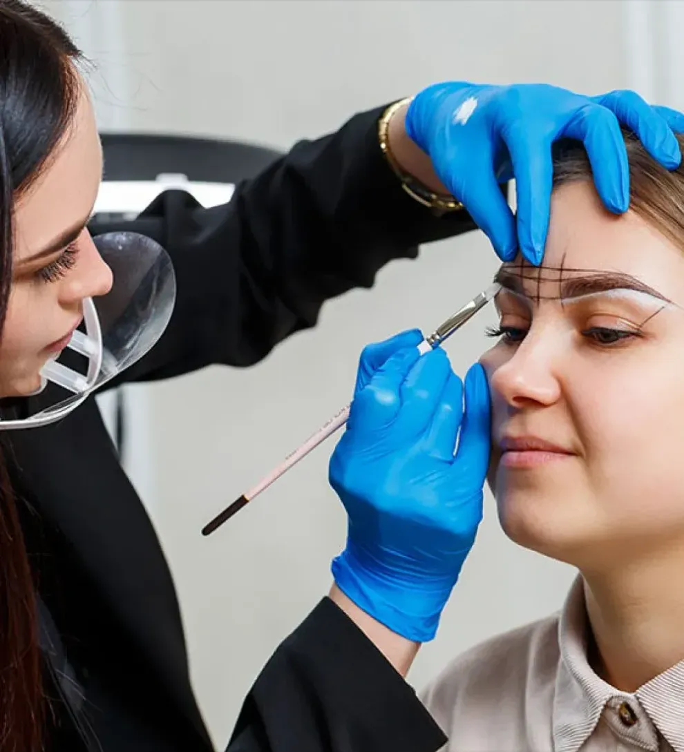 Cosmetologist shaping eyebrows with blue-gloved hands in a salon close-up