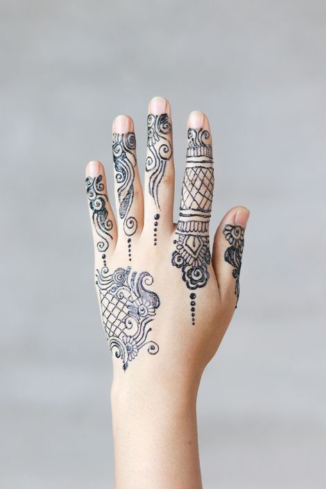 Hand with intricate black henna patterns on fingers and back against a gray background