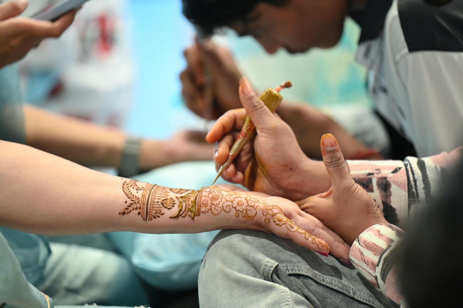 Hands applying henna on an outstretched arm during a close-up cultural celebration.