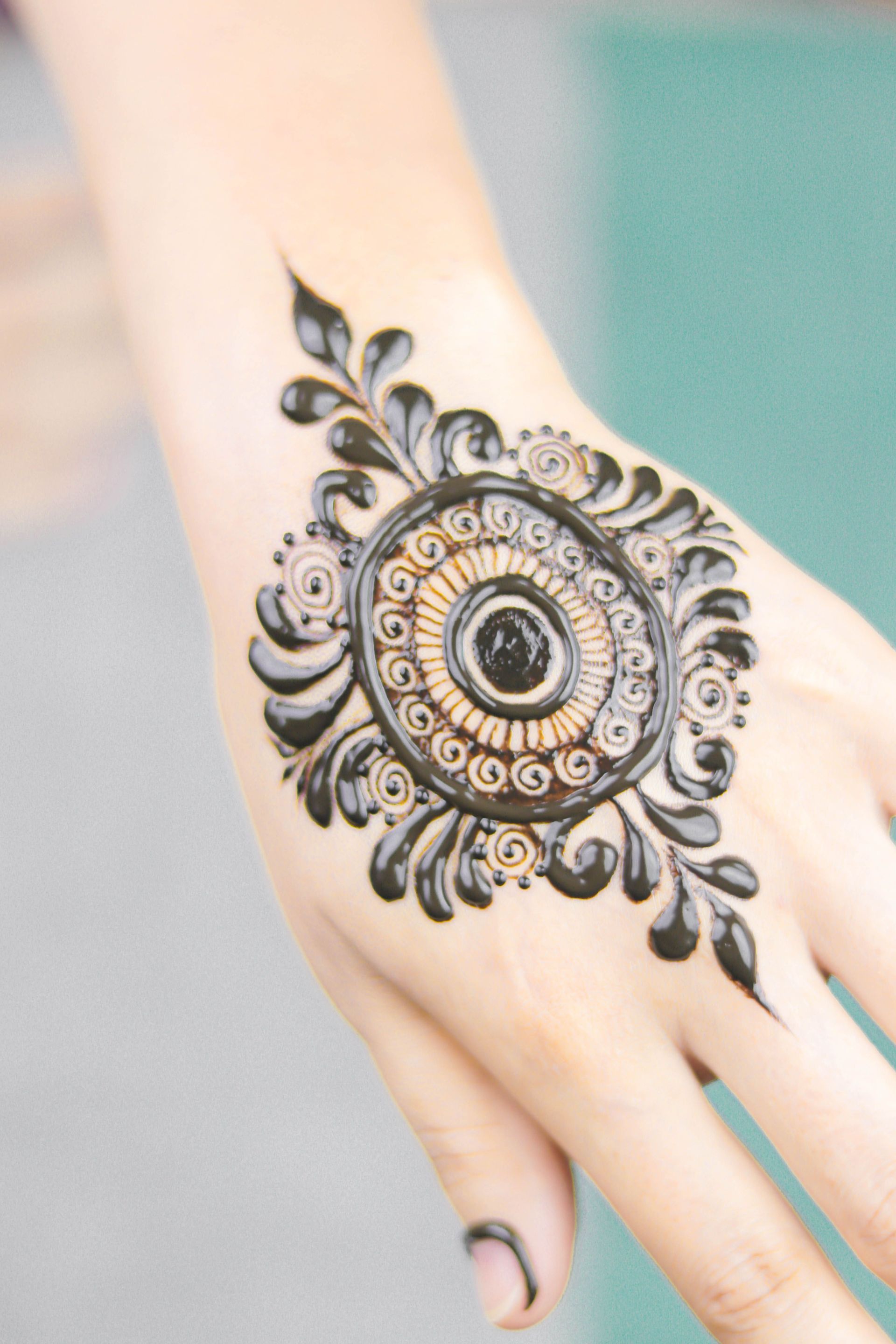 Hand with ornate black henna-style floral and circular design on the back of the hand