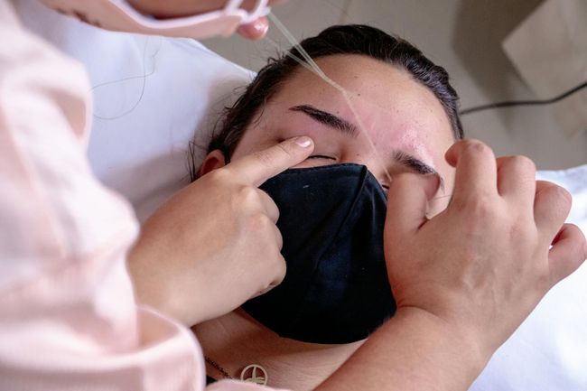 A clinician adjusts a black face mask on a patient lying down, with hands near the patient’s face.