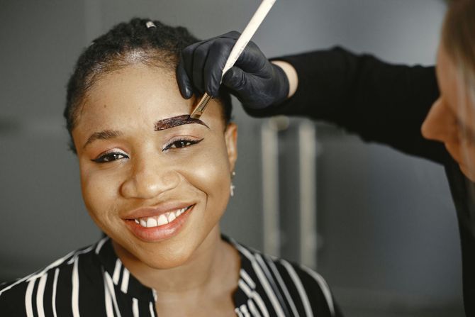 Woman smiling while having her eyebrow brushed by a makeup artist with a small brush