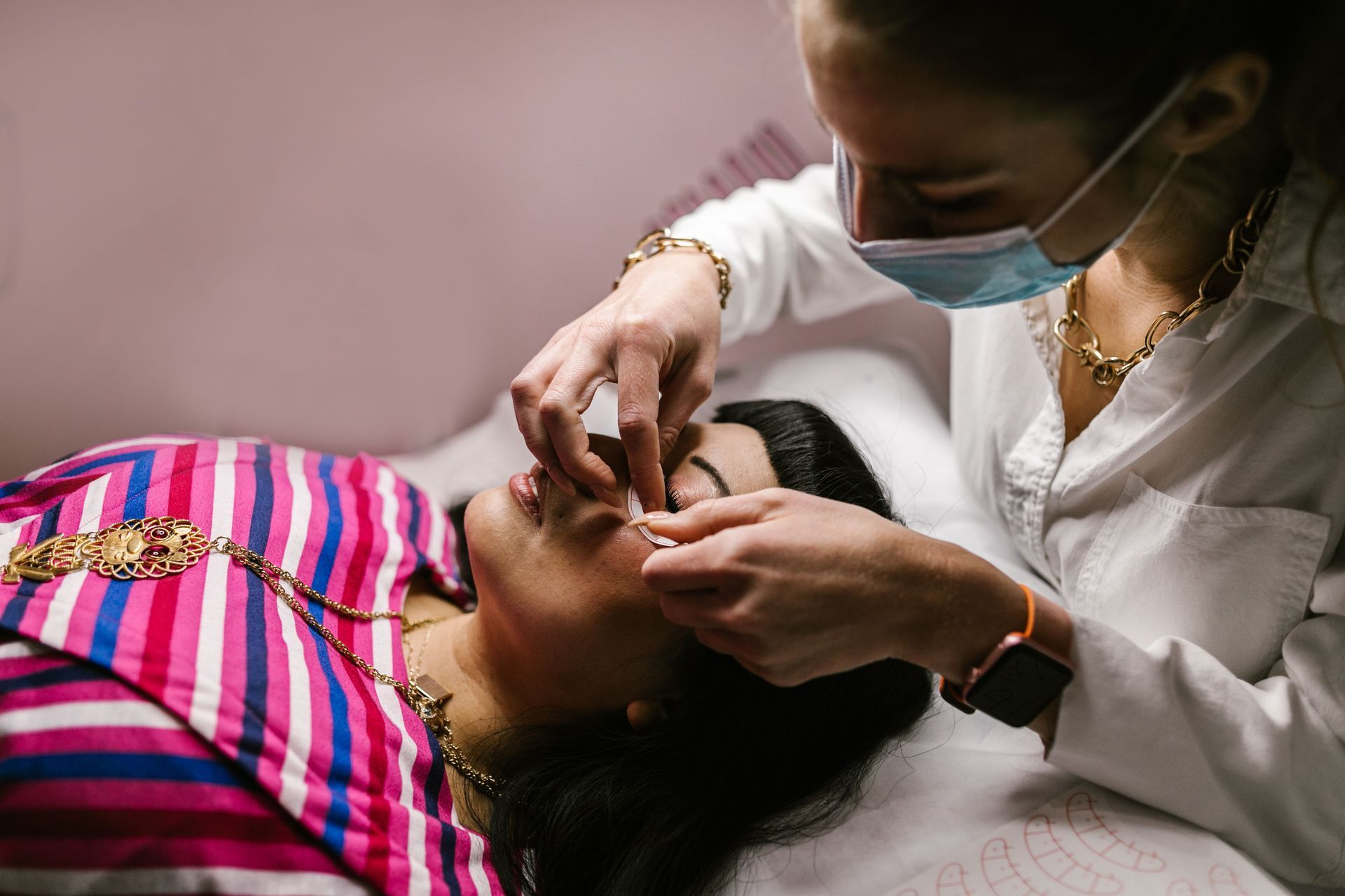 Beauty practitioner applying eyebrow treatment to a client lying on a bed