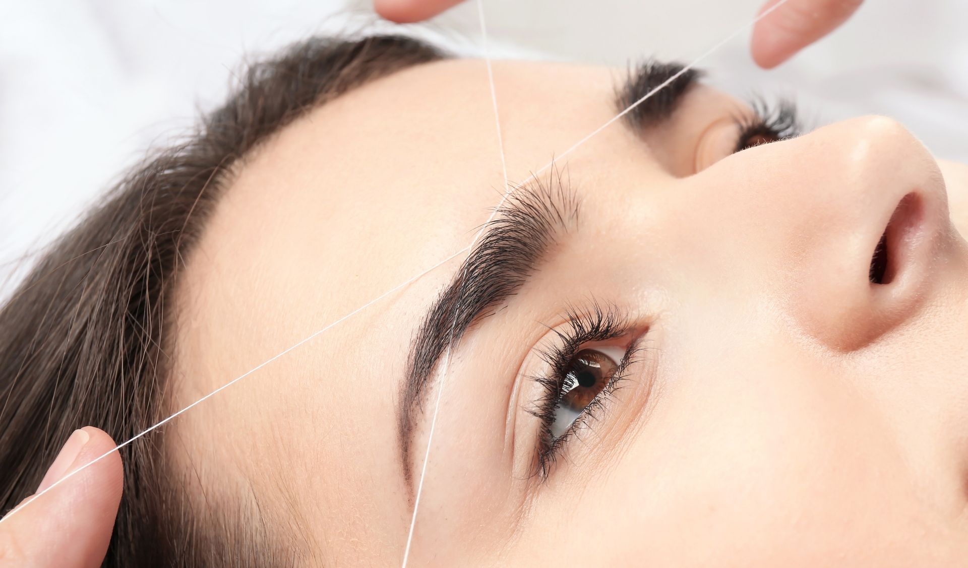 Close-up of hands adjusting glasses on a person lying down on a white surface