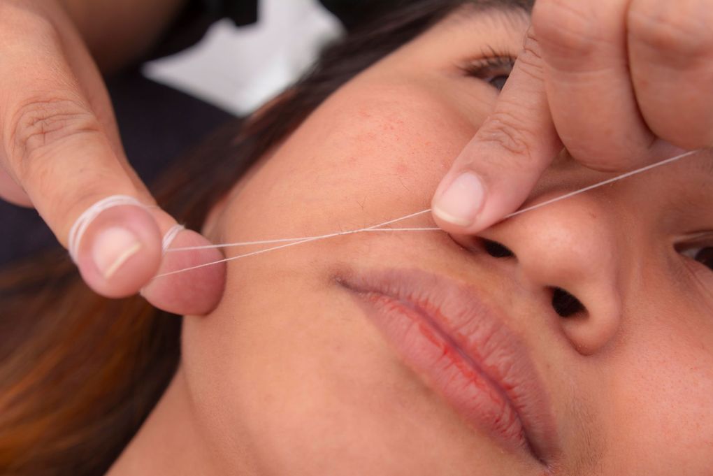 Person getting an eyebrow treatment with tweezers while lying down