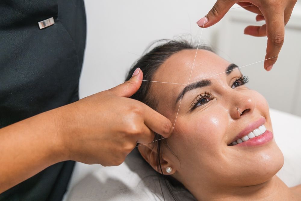 Cosmetologist applying eyebrow treatment to a client with eyes closed, wearing black gloves