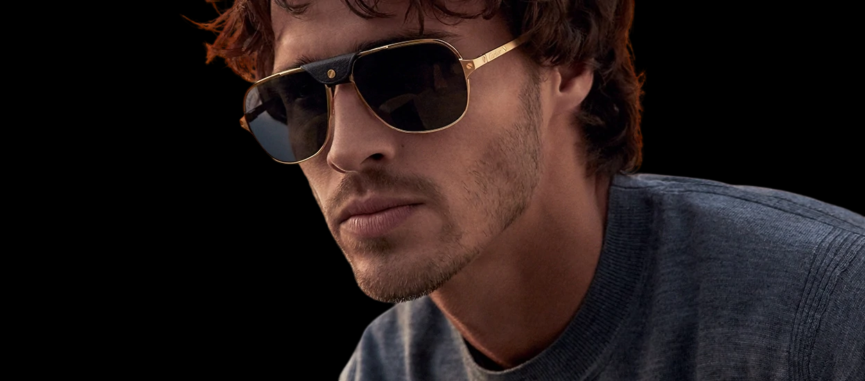A man wearing sunglasses and a sweater is looking at the camera.