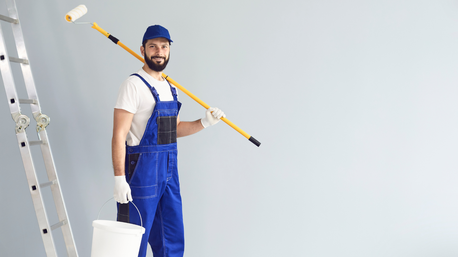 A man is standing on a ladder holding a paint roller and a bucket.