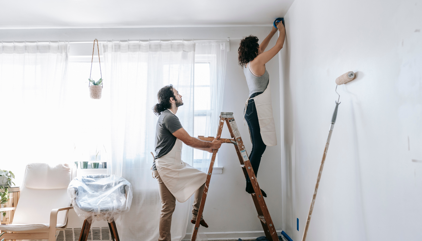 A man and a woman are painting a wall in a living room.