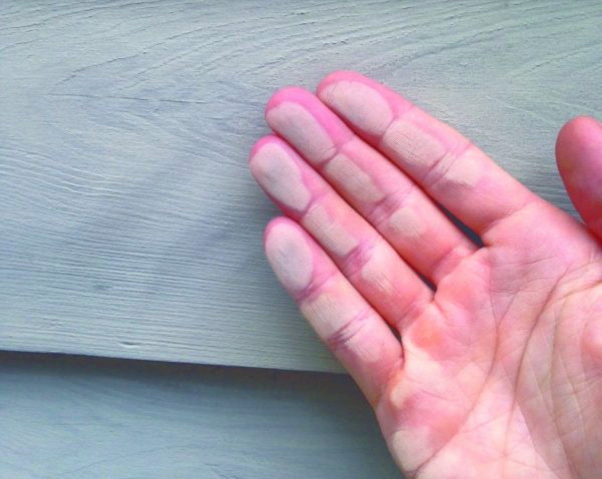 Hand with pink paint marks on fingertips, touching light gray painted wood.