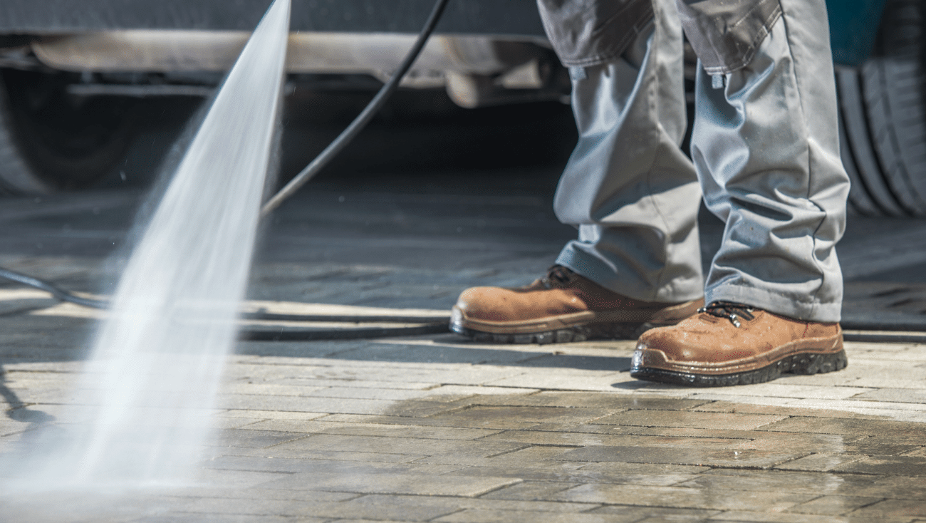 A person is using a high pressure washer to clean a concrete floor.